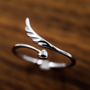 Peut inclure: Une bague en argent avec un design de cœur et d'aile. La bague est réglable et peut être portée à n'importe quel doigt.