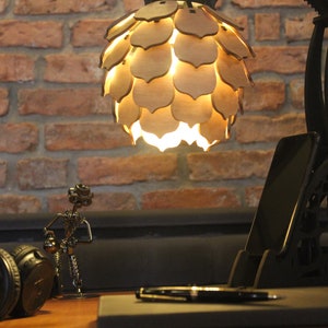 May include: A black desk lamp with a unique, articulated arm and a wooden, geometric shade. The lamp is on a desk with a phone, headphones, and a pen.