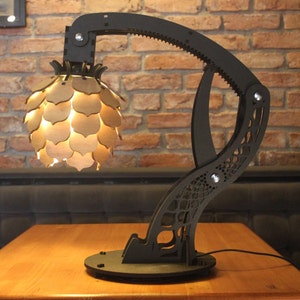May include: A black, articulated lamp with a wooden, geometric shade. The lamp is on a wooden table and has a black cord.