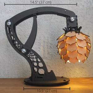 May include: A black and brown articulated lamp with a geometric base and a pineapple-shaped shade. The lamp is 14.5 inches tall, 12 inches wide, and 6 inches deep.