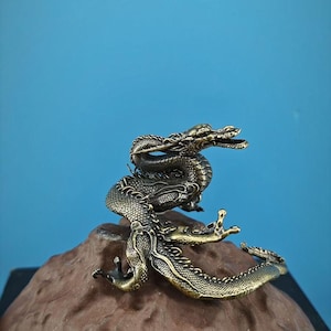 May include: A gold-colored dragon figurine curled up on a brown rock. The dragon has intricate details and a textured surface.