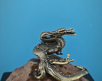 Puede incluir: Una figurita de dragón de color dorado enroscada en una roca marrón. El dragón tiene detalles intrincados y una superficie texturizada.