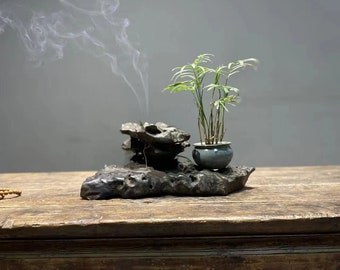May include: A wooden table with a small plant in a blue pot and a rock formation with smoke rising from it.