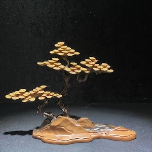 Puede incluir: Una escultura de bonsái de metal de color dorado con una base marrón. El árbol tiene muchas ramas y hojas, y la base tiene forma de roca.