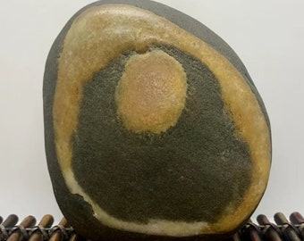May include: A smooth, round, gray stone with a large, light brown, circular pattern. The stone has a smaller, light brown, circular pattern inside the larger pattern.
