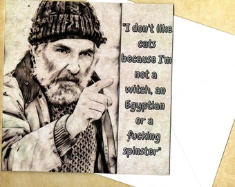 May include: A greeting card featuring a sepia-toned illustration of a bearded person wearing a knit cap and pointing forward. The text reads: I don't like cats because I'm not a witch, an Egyptian or a fucking spinster. The card is paired with an envelope.