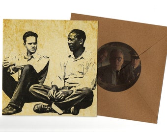 May include: A sepia-toned print of two men sitting and talking, with a brown envelope. The print shows two men in a prison setting. The envelope has a circular window showing a scene of men in suits.