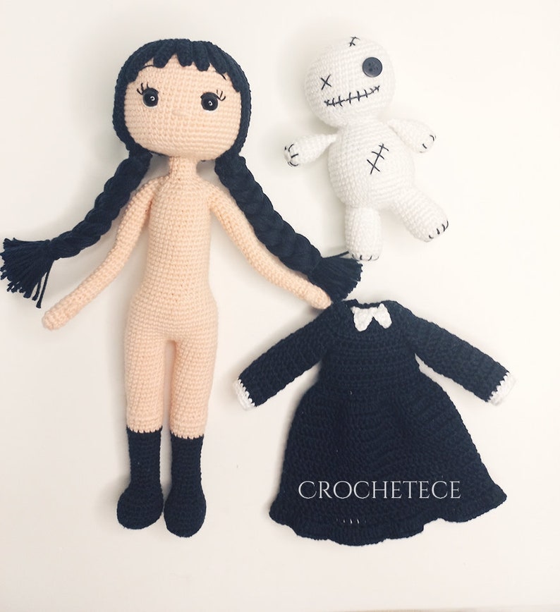 May include: Crocheted doll with black hair and a black dress, a white crocheted doll with black stitching, and a black dress with a white collar.