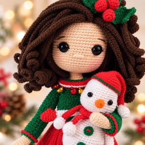 May include: A handcrafted crochet doll with dark brown curly hair, wearing a green dress with red trim and small gold bells. The doll holds a small white crochet snowman wearing a red hat and scarf, and has a holly leaf accessory in its hair.