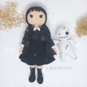 May include: A black and white crocheted doll with black hair in pigtails wearing a black dress and white collar. The doll is standing next to a white crocheted voodoo doll with black stitching and a single black button eye.