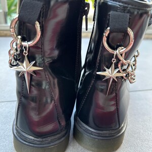 May include: A pair of black patent leather ankle boots with silver star charms and chain accents. The boots have a chunky black sole.