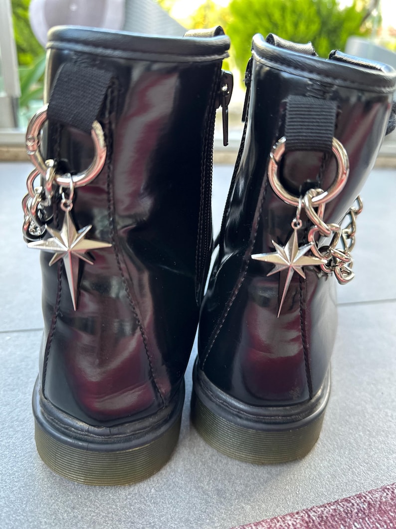 May include: A pair of black patent leather ankle boots with silver star charms and chain accents. The boots have a chunky black sole.