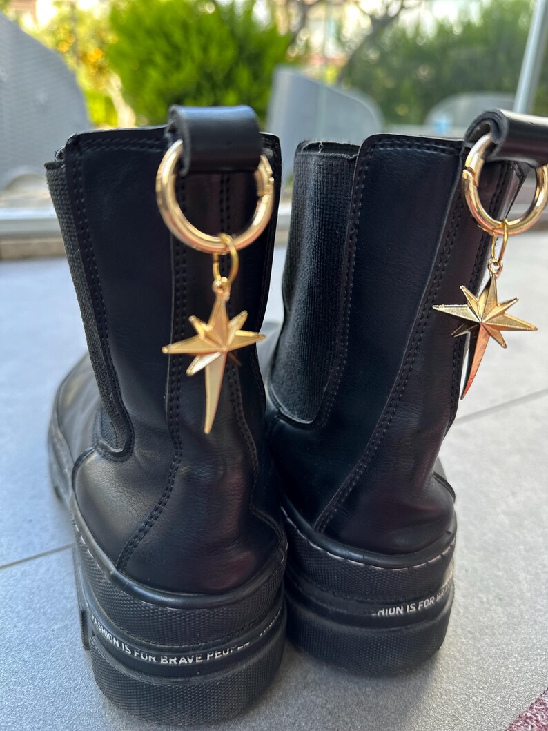 May include: Pair of black leather ankle boots with gold star charms attached to the top. The boots have a chunky platform sole and the text "Fashion is for brave people" is printed on the sole of one boot.