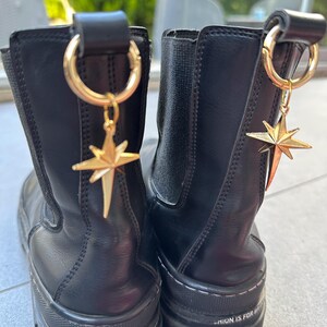 May include: Pair of black leather ankle boots with gold star charms attached to the top. The boots have a thick platform sole and the text "Fashion is for brave people" is printed on the side of each boot.