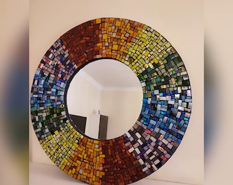 May include: A round mirror with a mosaic frame made of small, colorful glass tiles. The frame is arranged in a rainbow pattern, with red, orange, yellow, green, blue, and purple tiles. The mirror is perfect for adding a touch of color and whimsy to any room.
