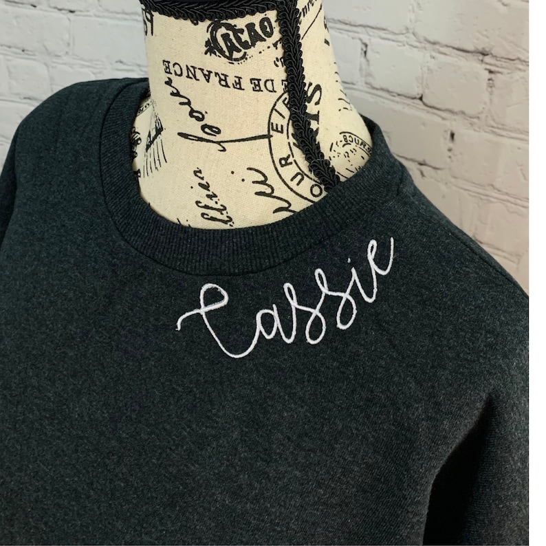 May include: A dark gray sweatshirt with the name "Cassie" embroidered in white on the front.