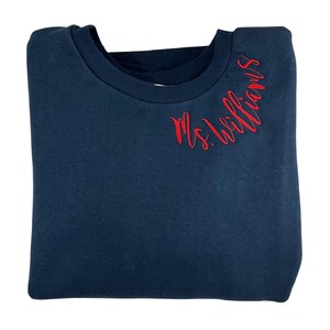 May include: A navy blue sweatshirt with the text "Ms. Williams" embroidered in red on the right shoulder.