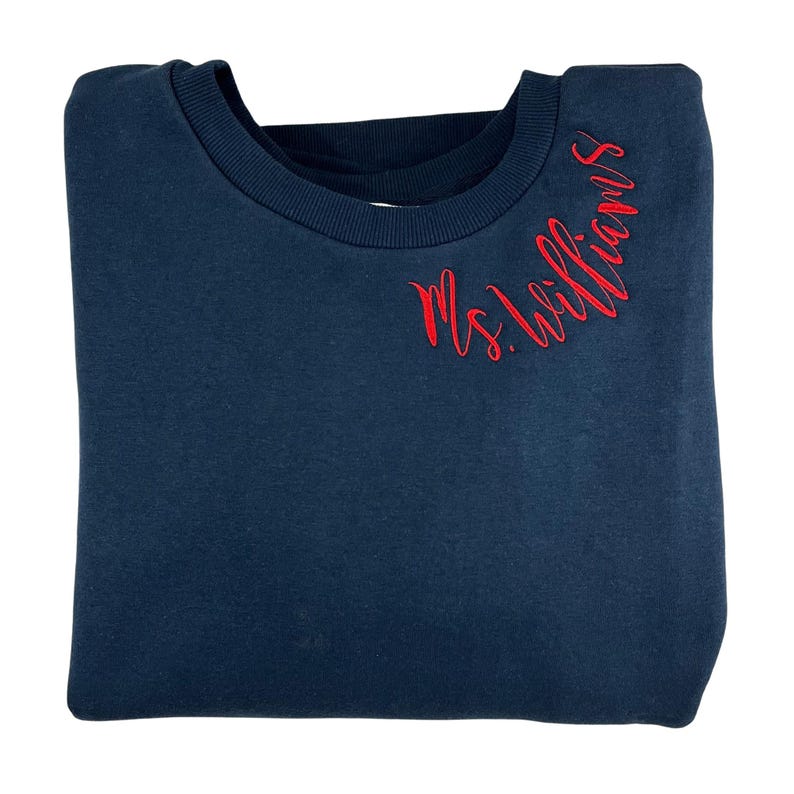 May include: A navy blue sweatshirt with the text "Ms. Williams" embroidered in red on the right shoulder.