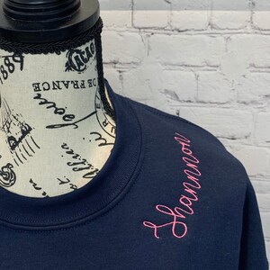 May include: A navy blue sweatshirt with the name "Shannon" embroidered in pink on the right shoulder.