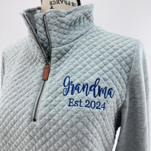 May include: Gray quilted zip-up sweatshirt with a blue embroidered design that says "Grandma Est. 2024".