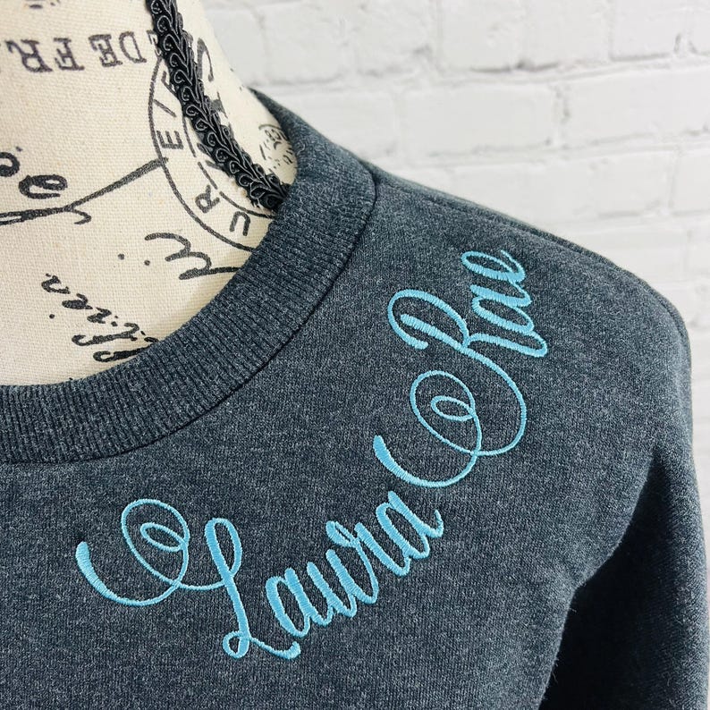 May include: A dark gray sweatshirt with a light blue embroidered design that says "Laura Co. Rae".