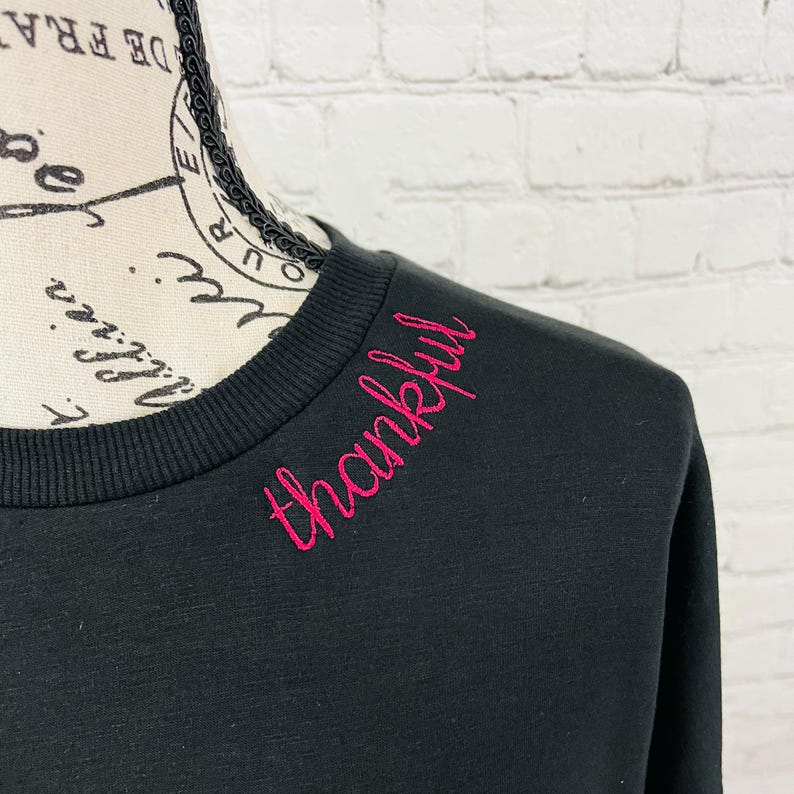 May include: Black sweatshirt with a pink embroidered word "thankful" on the neckline.