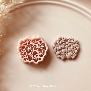 Puede incluir: Dos cortadores de galletas con forma de flor. Un cortador es un contorno detallado con un patrón floral, y el otro es un diseño floral en relieve. Ambos son de color rosa suave. La imagen incluye el texto "© 2024 Babycutters".