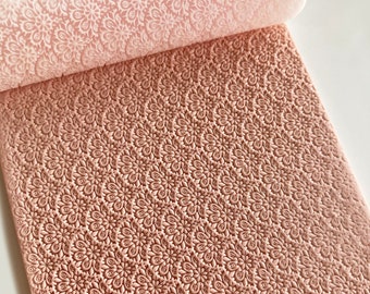 May include: A pink rolling pin with a detailed floral pattern. The rolling pin is partially unrolled, showing the intricate design. The pattern is embossed onto the surface, creating a textured effect. The image is a close-up, highlighting the details of the baking tool.