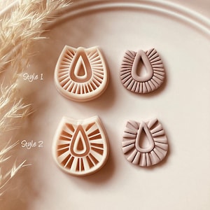 Peut inclure: Deux styles d'emporte-pièces en argile beige sont présentés. Le style 1 et le style 2 sont affichés, chacun avec une forme de goutte d'eau et des lignes rayonnantes. Le texte "Choose Style" et "© 2024 Babycutters" sont également visibles.