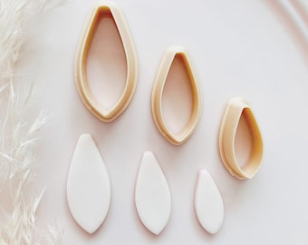 May include: A set of four beige petal-shaped cookie cutters and three white petal-shaped fondant cutouts. The cutters are in graduated sizes, with a smooth, rounded edge. The cutouts are also in graduated sizes, and are smooth and solid.