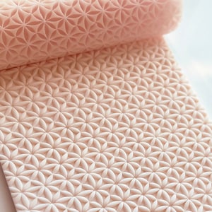 Könnte beinhalten: Eine hellrosa Teigrolle mit einem sich wiederholenden Blumenmuster. Die Rolle ist teilweise ausgerollt und zeigt das detaillierte Design. Die Oberfläche ist sauber und die Farbe ist durchgehend gleichmäßig.