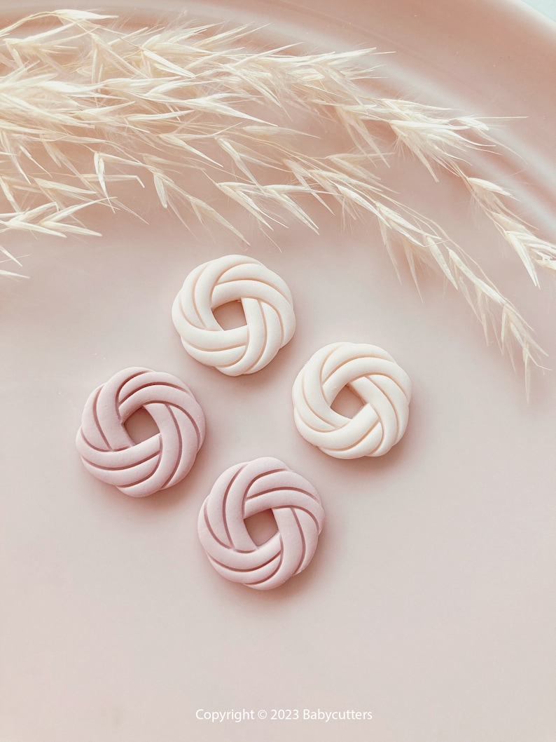 Puede incluir: Cuatro objetos decorativos circulares, blanquecinos y rosas, con un dise&ntilde;o tejido, est&aacute;n dispuestos sobre una superficie rosa. Los objetos son de diferentes tonos de rosa y blanco. Plantas beige secas y plumosas en el fondo.