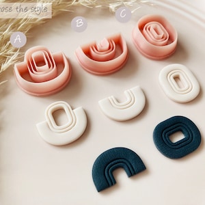 Può includere: Una selezione di taglierini in argilla polimerica in varie forme e colori. I taglierini sono in tonalità di rosa, bianco e blu navy. Il testo "Choose the style" è nella parte superiore dell'immagine, con le lettere A, B e C accanto ai diversi design.