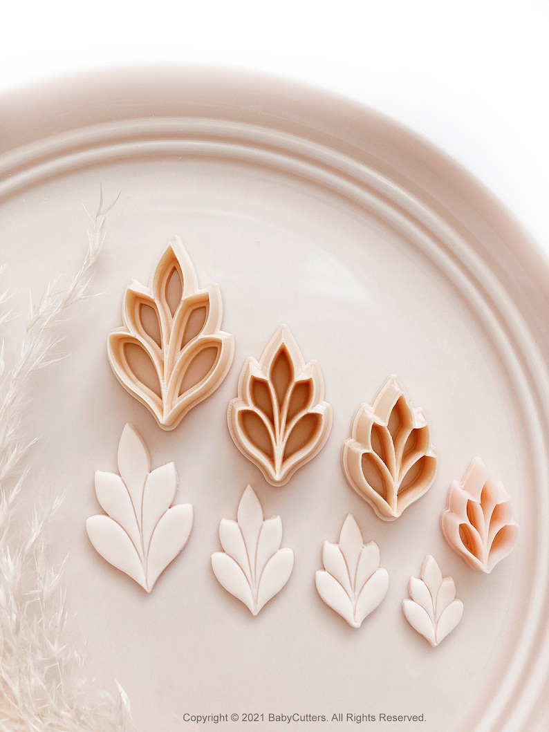 May include: A selection of leaf-shaped cookie cutters in different sizes. The cutters are in beige and white hues, displayed on a light pink plate. The image has a soft, natural aesthetic, suitable for baking or craft projects.