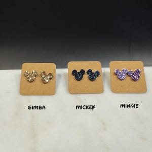 May include: Three pairs of glitter Mickey Mouse earrings on display cards. The earrings are gold, blue, and purple.