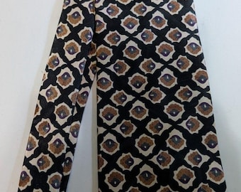 May include: A patterned necktie with a repeating geometric design. The tie features a black background with a pattern of brown, beige, and purple shapes. The tie is made of a smooth, possibly silk, material.