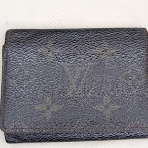 May include: A dark brown wallet with a textured surface. The wallet features a repeating pattern of interlocking logos in a lighter brown color. The wallet is closed and appears to be made of leather.
