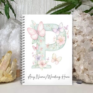 May include: A white spiral bound notebook featuring a watercolour illustration of the letter P surrounded by flowers and butterflies. The text "Any Name/Wording Here" is printed at the bottom of the notebook.