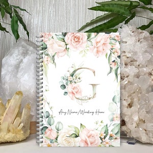 May include: A white spiral bound notebook with a floral design featuring pink and white roses, green leaves, and a gold letter G. The text "Any Name/Wording Here" is printed below the letter G.