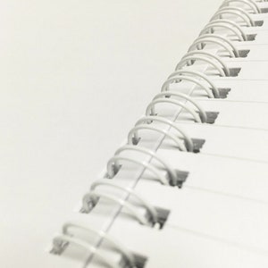 May include: Close-up of a white spiral bound notebook with a white background.