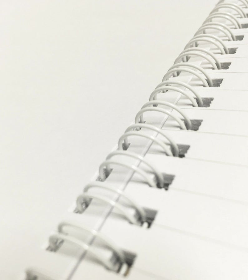 May include: Close-up of a white spiral bound notebook with a white background.