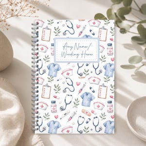 May include: A spiral-bound notebook featuring a white cover with a repeating watercolour pattern of medical supplies including stethoscopes, scrubs, nurse caps, syringes, and clipboards. A central rectangular label displays the text Any Name/ Wording Here.