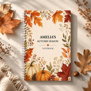 May include: A spiral-bound notebook with a cream-coloured cover featuring a border of autumn leaves, berries, and two pumpkins. The text on the cover reads AMELIA'S AUTUMN SEASON NOTEBOOK with a small maple leaf icon centred between the lines.