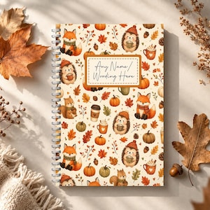 May include: A spiral-bound notebook featuring a repeating pattern of foxes, hedgehogs, squirrels, pumpkins, autumn leaves, and mugs of hot beverages. A central rectangular label with a brown border contains the text Any Name/Wording Here.