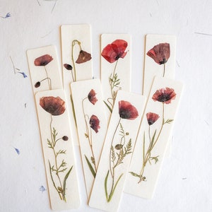 May include: Set of eight bookmarks featuring pressed red poppy flowers on white cardstock. Each bookmark has a different arrangement of the flowers and stems.
