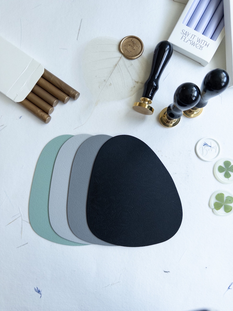 May include: A set of four round, textured coasters in shades of green, grey, and black. The coasters are arranged in a stack, with the black coaster on top. The coasters are made of a soft, absorbent material and are perfect for protecting your furniture from spills and scratches.