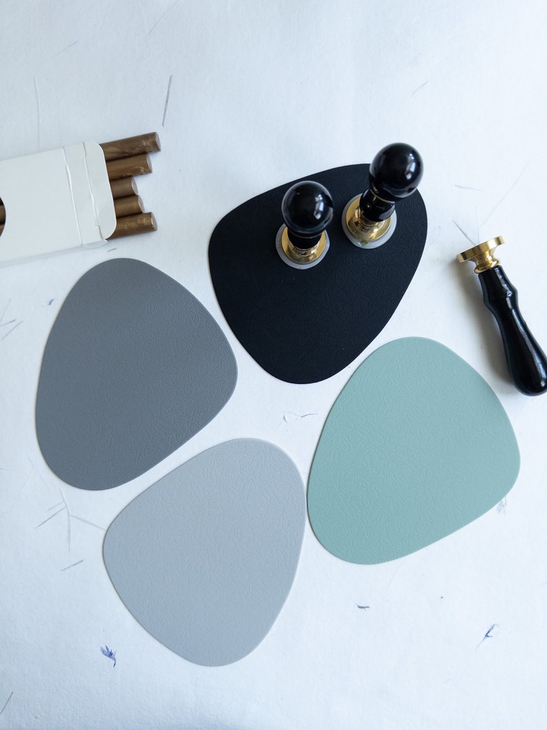 May include: Four grey and green round coasters with two black and gold wax seal stamps on a black coaster.