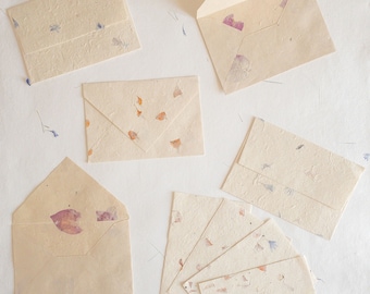 May include: A set of six handmade envelopes and note cards made from recycled paper with pressed flowers and petals. The envelopes and cards are beige with a variety of colors of flowers and petals.