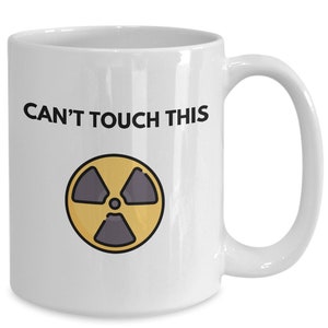 May include: White ceramic coffee mug with a black and yellow radiation symbol and the text "CAN'T TOUCH THIS".