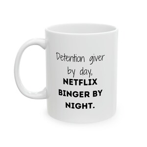 May include: White ceramic coffee mug with black text that reads "Detention giver by day, NETFLIX BINGER BY NIGHT."